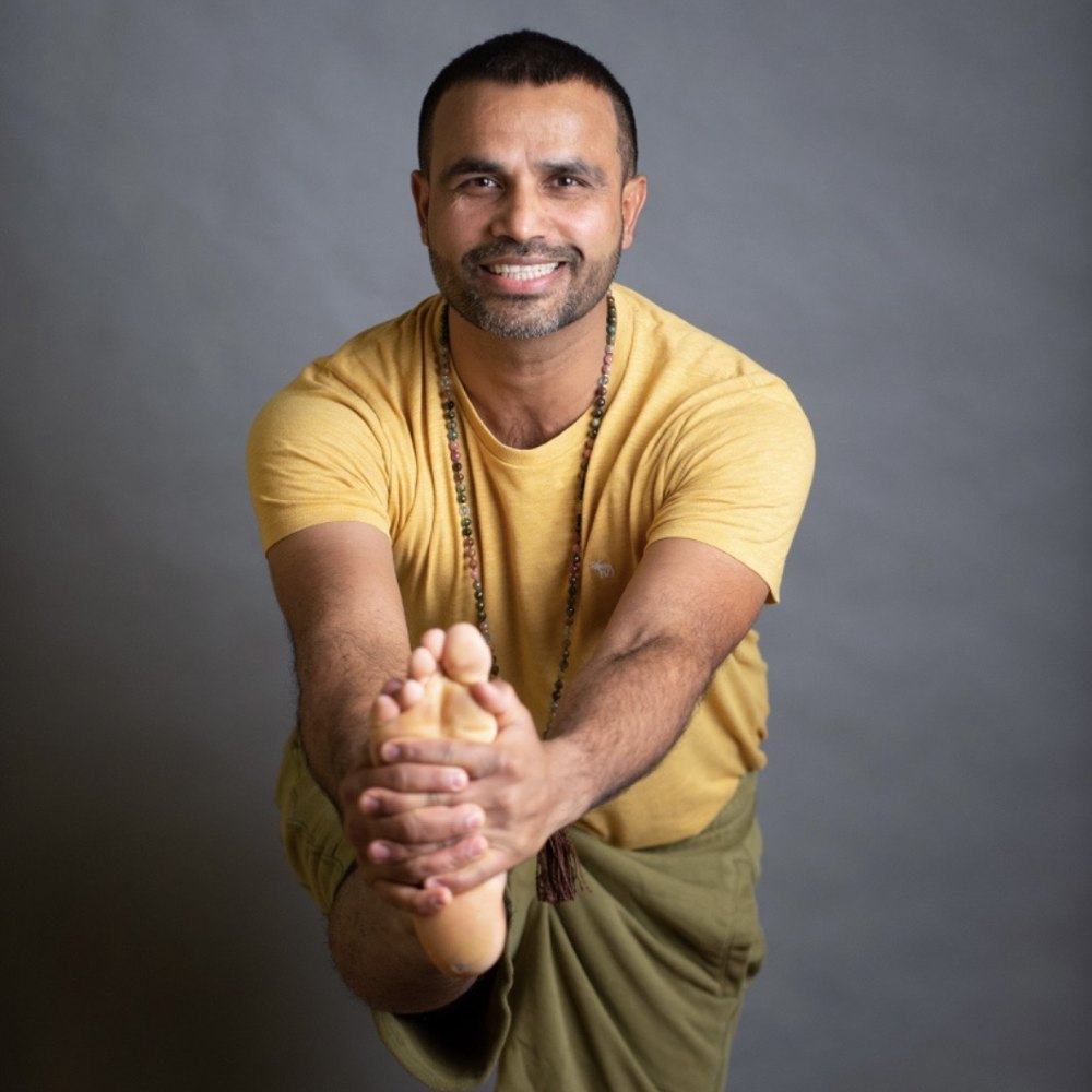 Yogi Ananda smiling in a standing leg-stretch pose